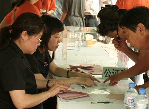 Two notary officials check the documents of voters at the venue for a vote on demolishment and reconstruction of old buildings in Juixiaqiao Sub-district in Beijing, June 9, 2007. Local government and the real estate developer jointly organize the vote on Saturday to see if majority residents of over 5000 families accept the new compensation policy after failed attempts to reach an agreement through other ways. Both notary officials and supervisors are invited to monitor the vote that runs from 9 a.m. to 9 p.m. at six ballot booths. [Sun Yuqing/www.ttav89.com]